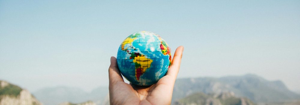 Person Holding World Globe Facing Mountain