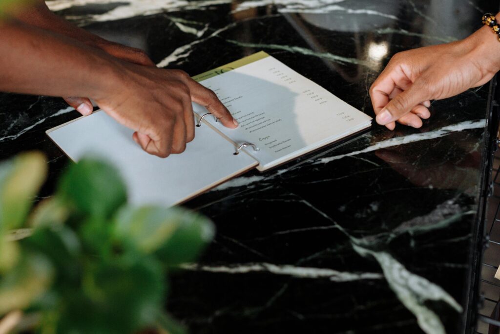 Hands pointing at menu on black marble counter inside a shop.