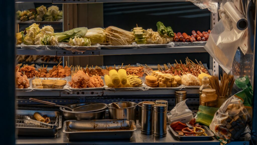 Vibrant street food stall with diverse skewers, vegetables, and condiments on display.